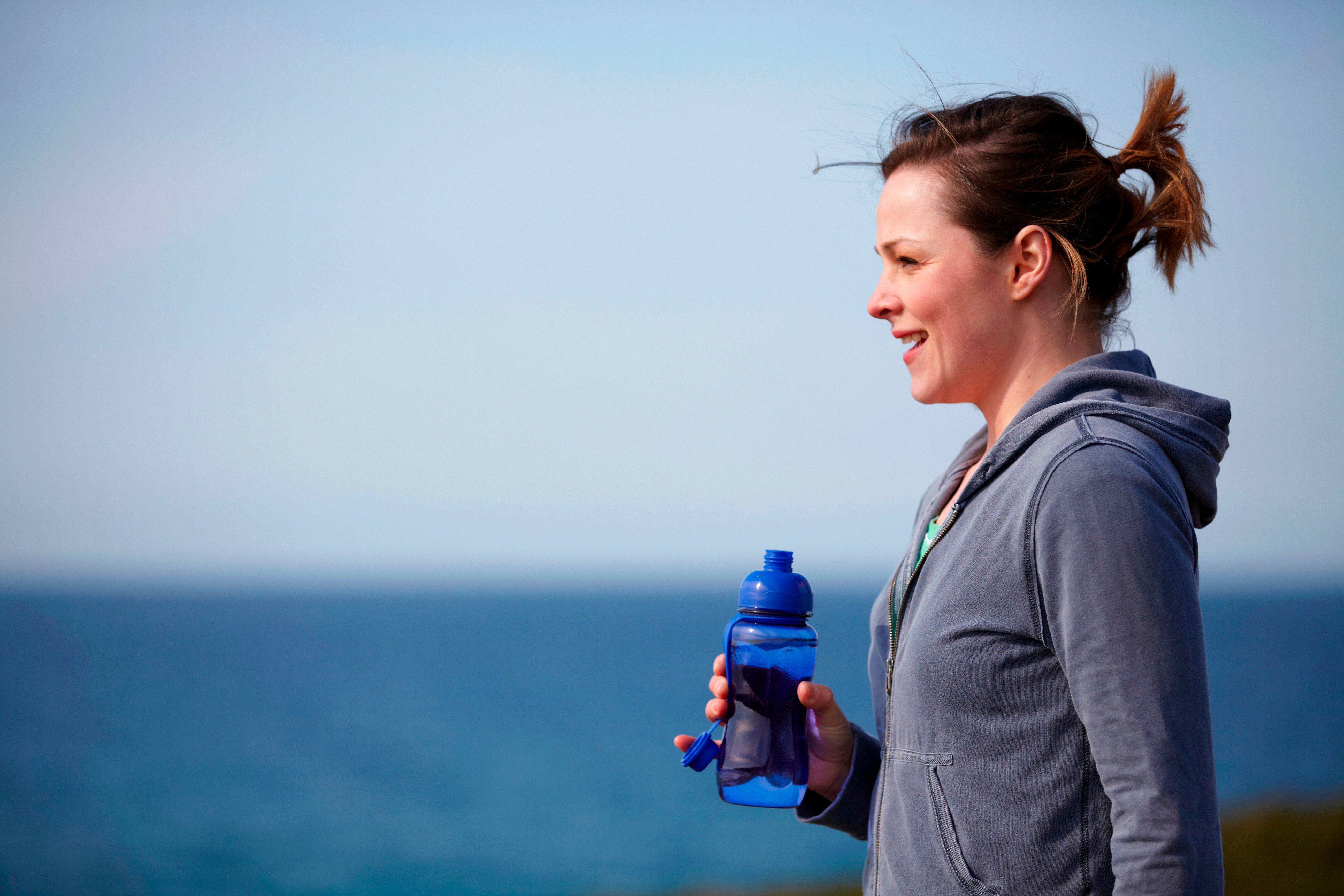 woman drinks water looking out to sea - healthy lifestyle
