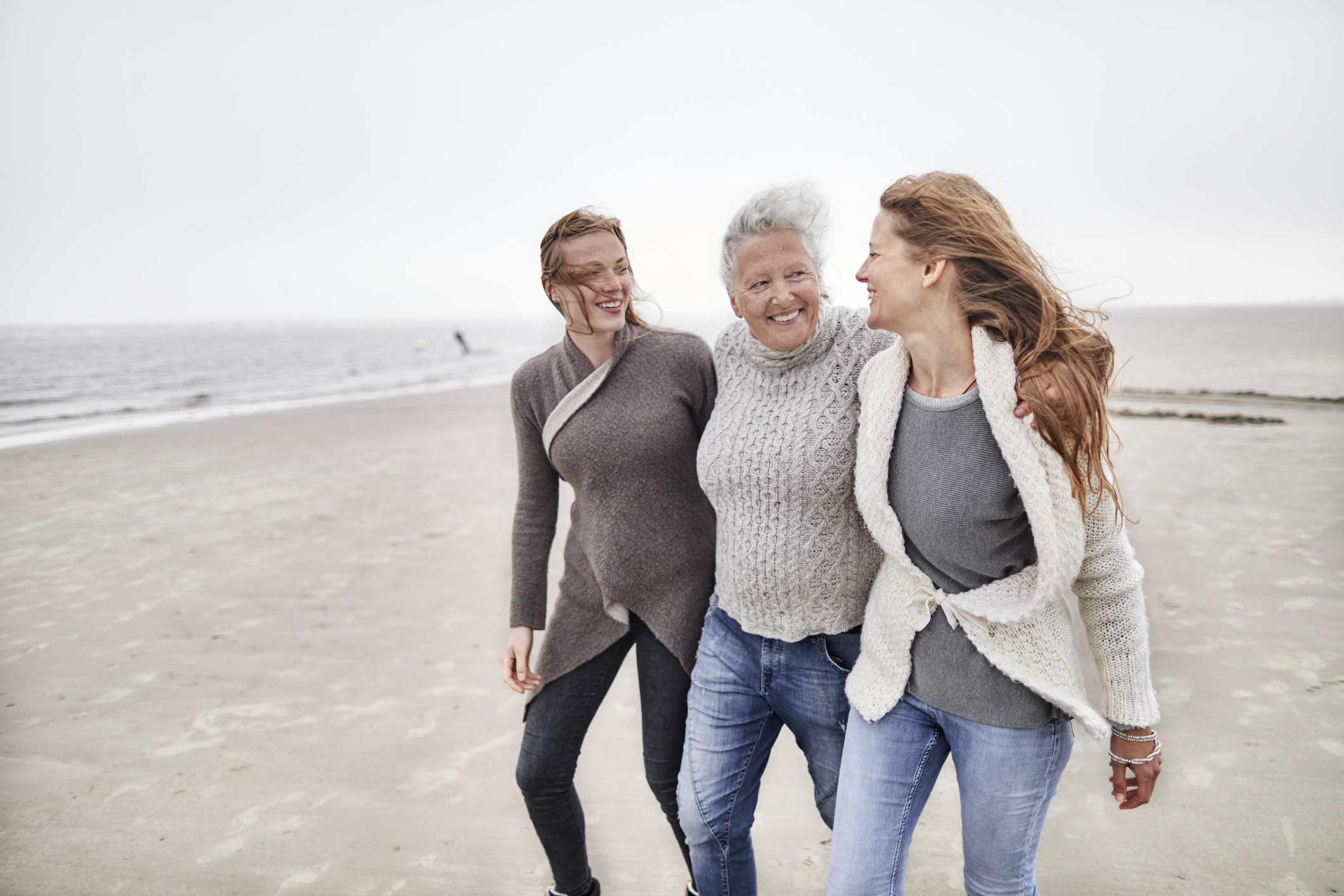 Three generations of women walk along a windy beach